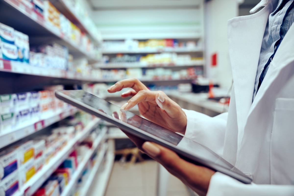 Pharmacist using a mobile device by a shelf of medicine