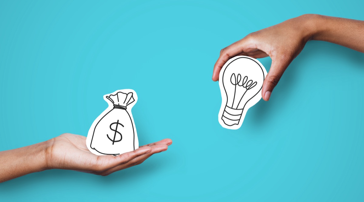 Hands holding cutout images of a money bag and a lightbulb